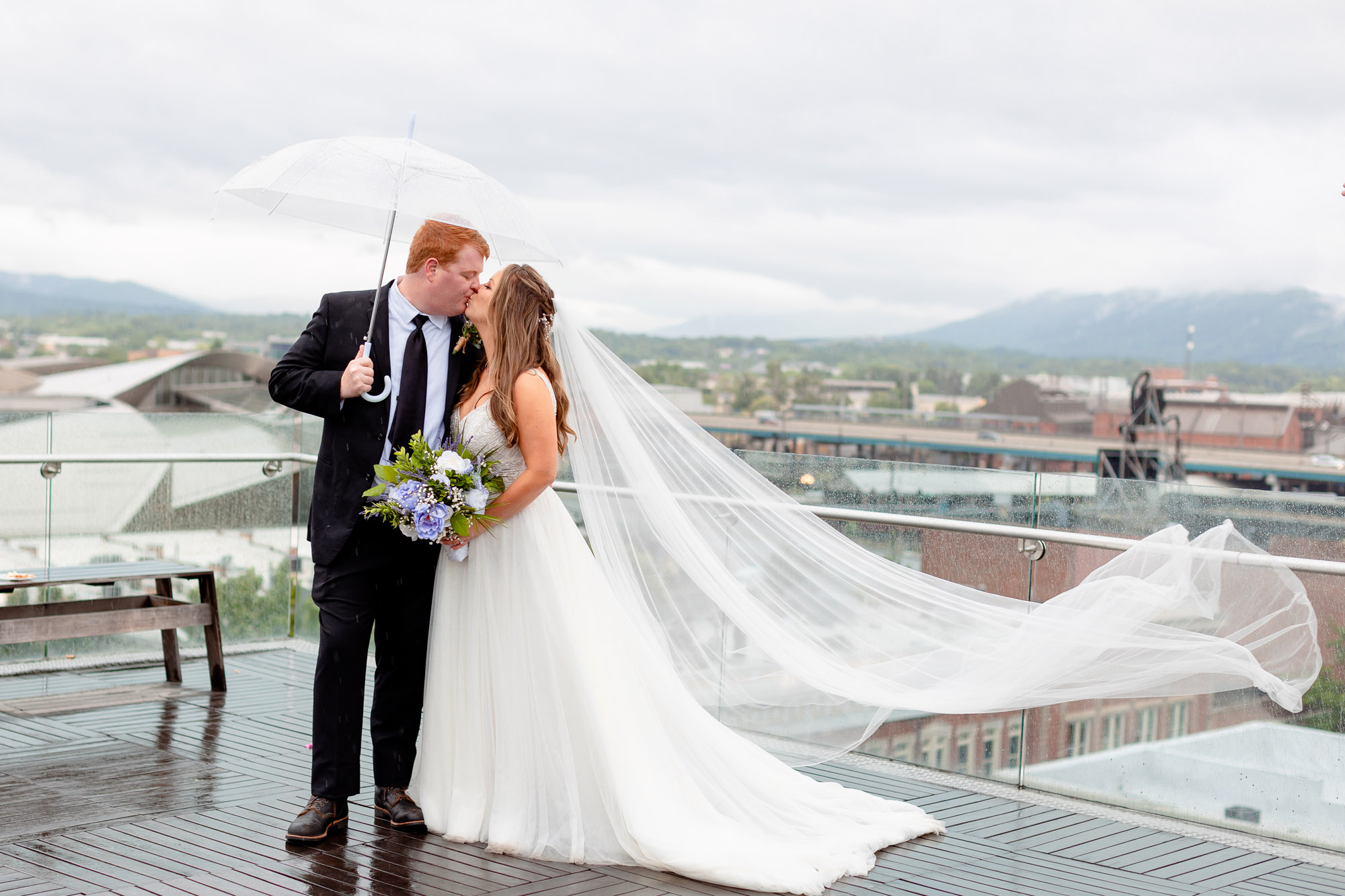 Bride and Groom Kissing Under Umbrella in Front of Roanoke City Buildings