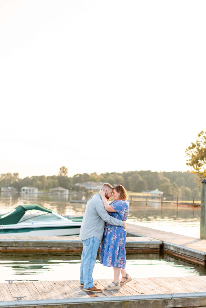 A newly engaged couple snuggle touching foreheads while standing on a boat dock at sunset